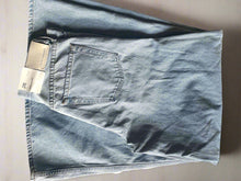 Load image into Gallery viewer, Folded light blue jeans with a brand tag on a textured surface