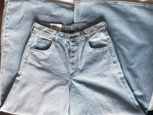 Load image into Gallery viewer, Folded light blue jeans on a wooden surface