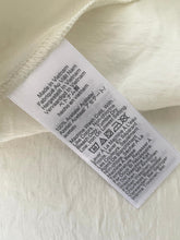 Load image into Gallery viewer, Clothing label with text on a beige fabric background