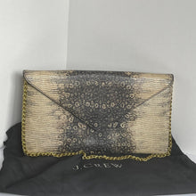 Load image into Gallery viewer, A rectangular clutch bag with a snakeskin pattern in black and beige, featuring gold chain trim and a diagonal flap closure, shown next to a black dust bag with gold lettering.