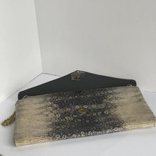 Load image into Gallery viewer, A textured clutch purse with a black and gold gradient pattern, featuring a black leather-like flap, gold-tone hardware, and a gold tassel zipper pull, shown on a plain white background.