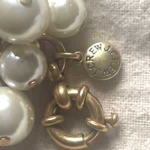 Gold and pearl earring with 'J.Crew' label on a textured fabric background