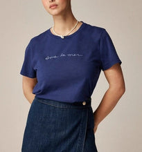 Load image into Gallery viewer, Woman wearing a blue t-shirt with text and a denim skirt on a beige background