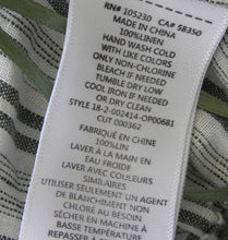 Load image into Gallery viewer, Close-up of a white fabric care label sewn onto a striped green and white textile, with printed text showing product details and care instructions.