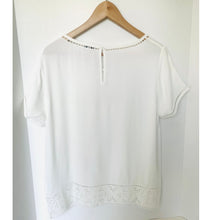 Load image into Gallery viewer, White blouse with lace details on a wooden hanger against a white background