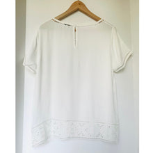 Load image into Gallery viewer, White blouse with lace details on a wooden hanger against a white background