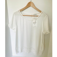 Load image into Gallery viewer, White blouse with lace details on a wooden hanger against a white background