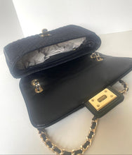 Load image into Gallery viewer, A black leather handbag with gold-tone hardware, shown open to display its interior and flap. The bag features a quilted texture on the exterior and a smooth finish on the interior flap, with a black-and-gold chain strap and a rectangular gold-tone clasp.