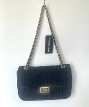 Load image into Gallery viewer, A black quilted Karl Lagerfeld shoulder bag with a gold-tone turn-lock closure and a silver-tone chain strap, shown hanging against a plain white wall with its brand tag attached.