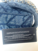 Load image into Gallery viewer, A close-up of a blue denim-textured handbag with a gold chain strap, alongside a black product care tag with white text.