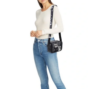 Person wearing a white sweater and blue jeans with a black crossbody bag featuring a logo.