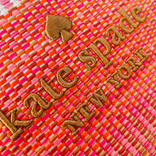 Load image into Gallery viewer, Close-up of a woven bag with 'kate spade new york' embroidery on a pink and orange patterned background.