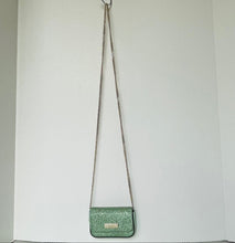 Load image into Gallery viewer, Green glittery handbag with a chain strap hanging on a white wall.
