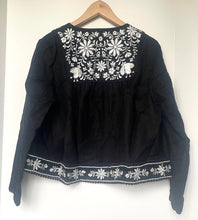 Load image into Gallery viewer, Black blouse with white embroidery on a hanger against a white background
