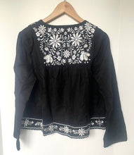 Load image into Gallery viewer, Black blouse with white floral embroidery on a wooden hanger against a white background