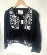 Load image into Gallery viewer, Black blouse with white floral embroidery on a hanger against a white background