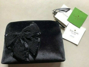 Black clutch bag with a bow detail on a beige surface, accompanied by Kate Spade cards.