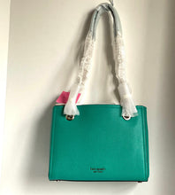 Load image into Gallery viewer, A teal green pebbled leather handbag with white protective plastic wrapping on its handles, hanging from a metal hook against a plain off-white wall. The brand name 'Kate Spade New York' is printed in gold on the lower front.