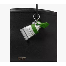Load image into Gallery viewer, Green bottle-shaped keychain on a black handbag with 'kate spade' branding.