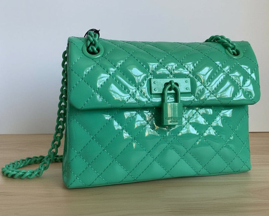 Green quilted handbag with a chain strap on a wooden surface.