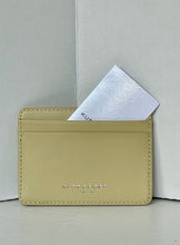 Load image into Gallery viewer, A light beige leather card holder wallet with silver-tone debossed branding, shown with a white card partially inserted, set against a neutral light gray background.