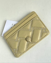 Load image into Gallery viewer, A small quilted card holder or wallet in light beige leather with a central metallic clasp, shown on a plain light background with a small white tag partially visible.