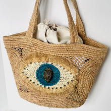 Load image into Gallery viewer, Woven bag with decorative eye design on a white background