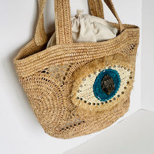 Load image into Gallery viewer, Woven bag with decorative eye design on a white background