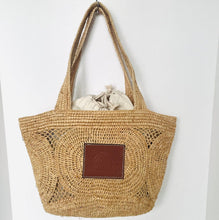 Load image into Gallery viewer, Woven straw bag with a brown leather patch on a white background