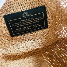 Load image into Gallery viewer, Black label with gold text on a woven straw surface