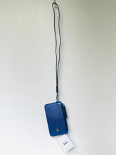 Load image into Gallery viewer, A blue textured leather phone pouch with a black wrist strap, shown hanging against a plain light wall with a white product tag attached.