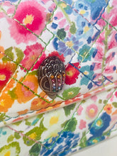 Load image into Gallery viewer, Close-up of a colorful floral-patterned fabric with a decorative brooch.