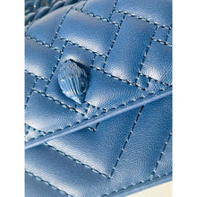Load image into Gallery viewer, Close-up of a blue quilted handbag with a shell detail on a white background