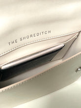 Load image into Gallery viewer, Close-up of a beige handbag with 'The Shoreditch' branding.