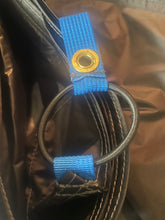 Load image into Gallery viewer, Close-up of a brown bag with a black elastic loop and blue webbing straps secured by gold metal grommets.