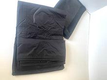 Load image into Gallery viewer, A pair of black lightweight fabric pants or shorts folded inside a white box, with a matching black fabric sleeve or cover placed behind them.