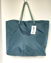 Load image into Gallery viewer, A teal blue reusable shopping tote bag with green and white patterned rope handles, hanging on a hook against a plain white wall. A white brand tag is attached to the side.