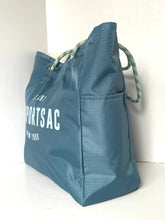 Load image into Gallery viewer, A blue nylon tote bag with white printed text reading 'LAST SPORTSAC NEW YORK' and green-and-white braided rope handles, photographed against a plain white wall and floor.
