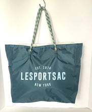 Load image into Gallery viewer, A teal blue Lesportsac tote bag with white printed text and green-and-white patterned rope handles, hanging against a plain white wall.
