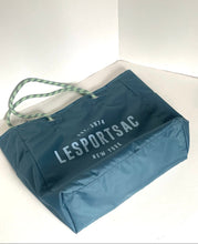Load image into Gallery viewer, A blue LeSportsac tote bag with white printed branding and green-and-white rope handles, photographed on a white surface in a corner setting.