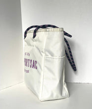 Load image into Gallery viewer, An off-white canvas tote bag with purple text reading 'SPORTSAC' and 'EST. 2014 NEW YORK' on the front, featuring dark purple patterned drawstring handles, set against a plain white background.