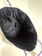 Load image into Gallery viewer, Close-up of the inside of a bucket bag or tote, showing a black fabric lining and a patterned strap in pink, purple, and blue.