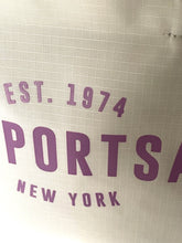 Load image into Gallery viewer, Close-up of a light beige or off-white textured fabric surface with purple printed text reading 'EST. 1974', 'PORTS', and 'NEW YORK'.