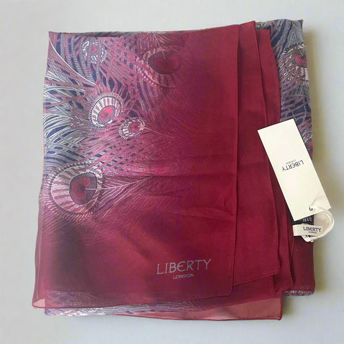 Red scarf with peacock feather pattern and 'Liberty London' tag on a white background