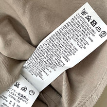 Load image into Gallery viewer, Close-up of a label on beige fabric with text and symbols.