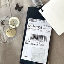 Load image into Gallery viewer, Clothing tag with product details on a textured surface