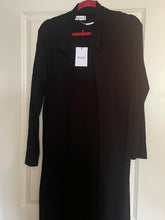 Load image into Gallery viewer, A black long-sleeve collared coat or duster hanging on a red hanger against a white paneled door, with a white retail tag attached.