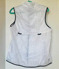 Load image into Gallery viewer, White sleeveless jacket with black trim hanging on a green hanger against a white wall.