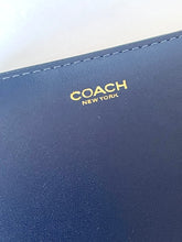 Load image into Gallery viewer, Close-up of a navy blue leather wallet or notebook cover with gold foil 'COACH NEW YORK' branding and visible stitching along the edge.