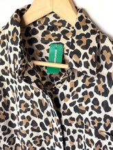 Load image into Gallery viewer, A leopard print button-up shirt hanging on a wooden hanger, featuring a beige base with black and brown spots. A green brand tag reading 'SIMON' is visible at the collar.